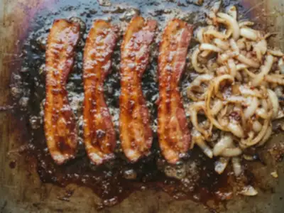 Concept imagery: glossy amber candied bacon and golden grilled onion caramelizing on the griddle
