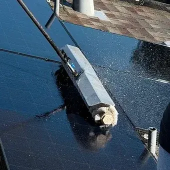Close view of the soft brush head pressed flat against the panel glass with water running off the surface.