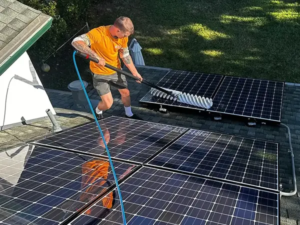 A Total Solar Cleaning technician washing a rooftop solar array with a water-fed pole and a soft brush head.
